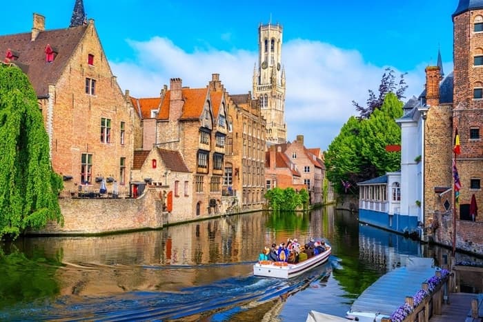 Tour boat on a scenic Bruges canal with historic brick buildings and the Belfry tower.